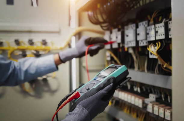Serwisant wykonujący pomiary elektryczne miernikiem w szafie sterowniczej.